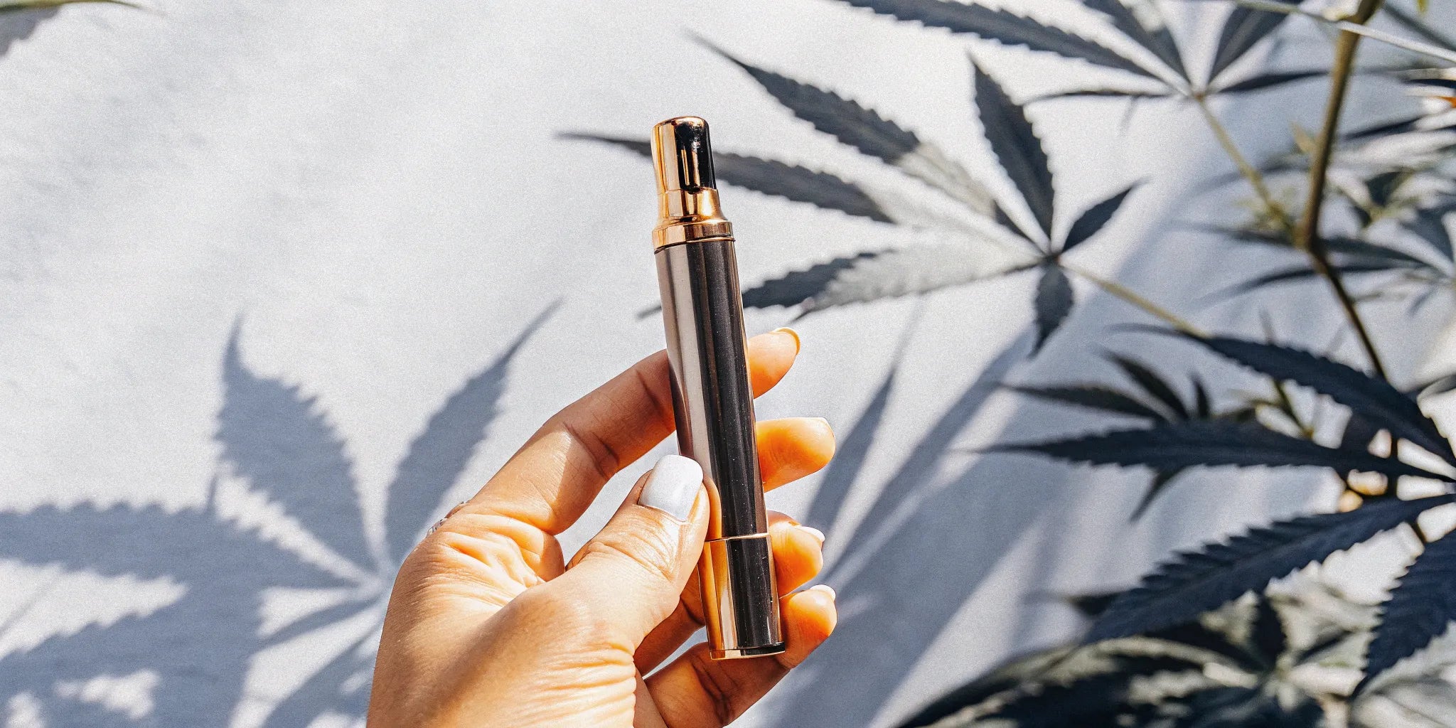 Hand holding a THCA pen in front of cannabis leaves, a top choice for buying pens online.