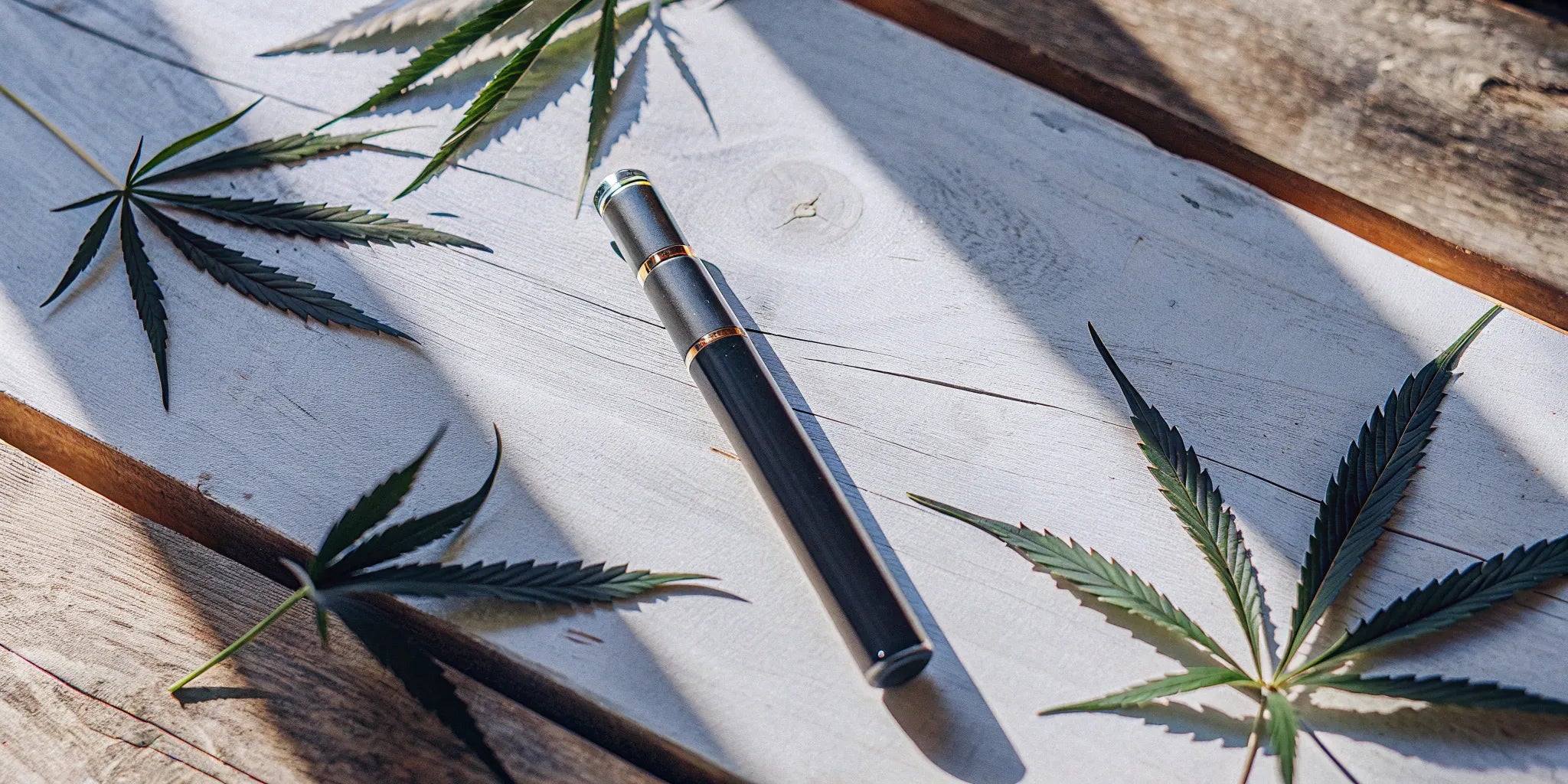 A modern delta 8 pen resting on a wooden table next to hemp leaves.