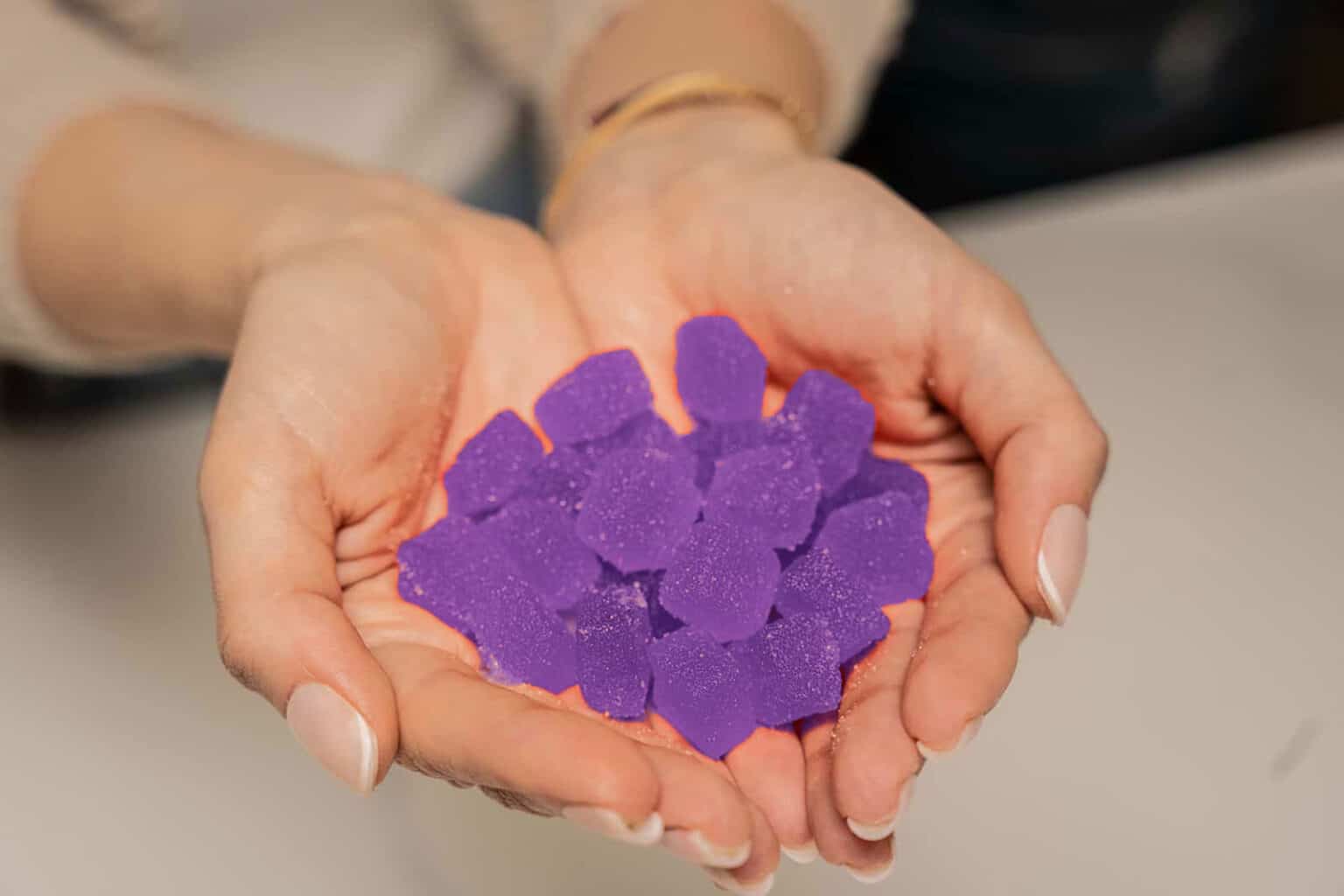 A person's hands holding a pile of purple THC gummies.