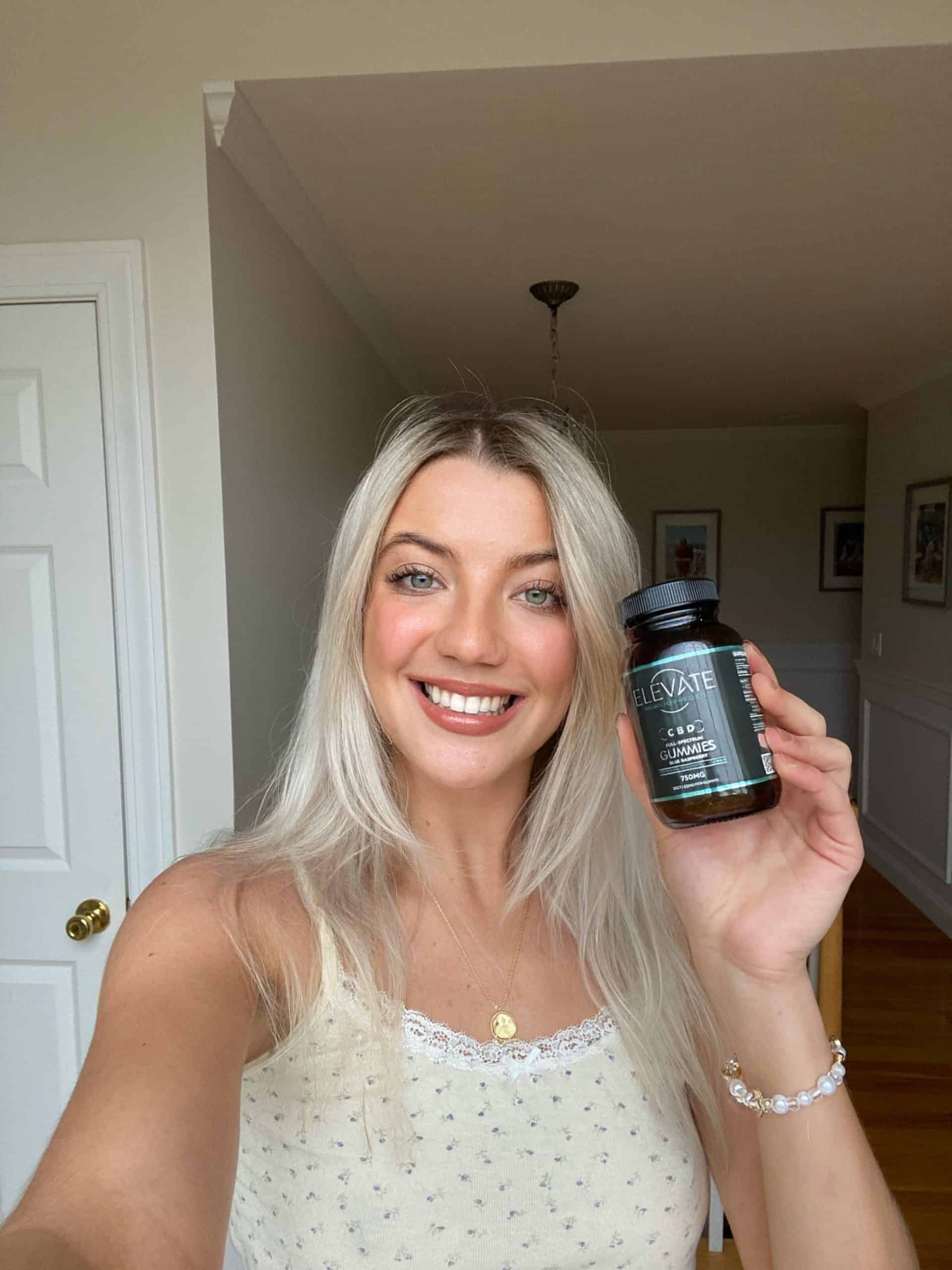 A woman smiling and holding Elevate product bottle in a bright room.