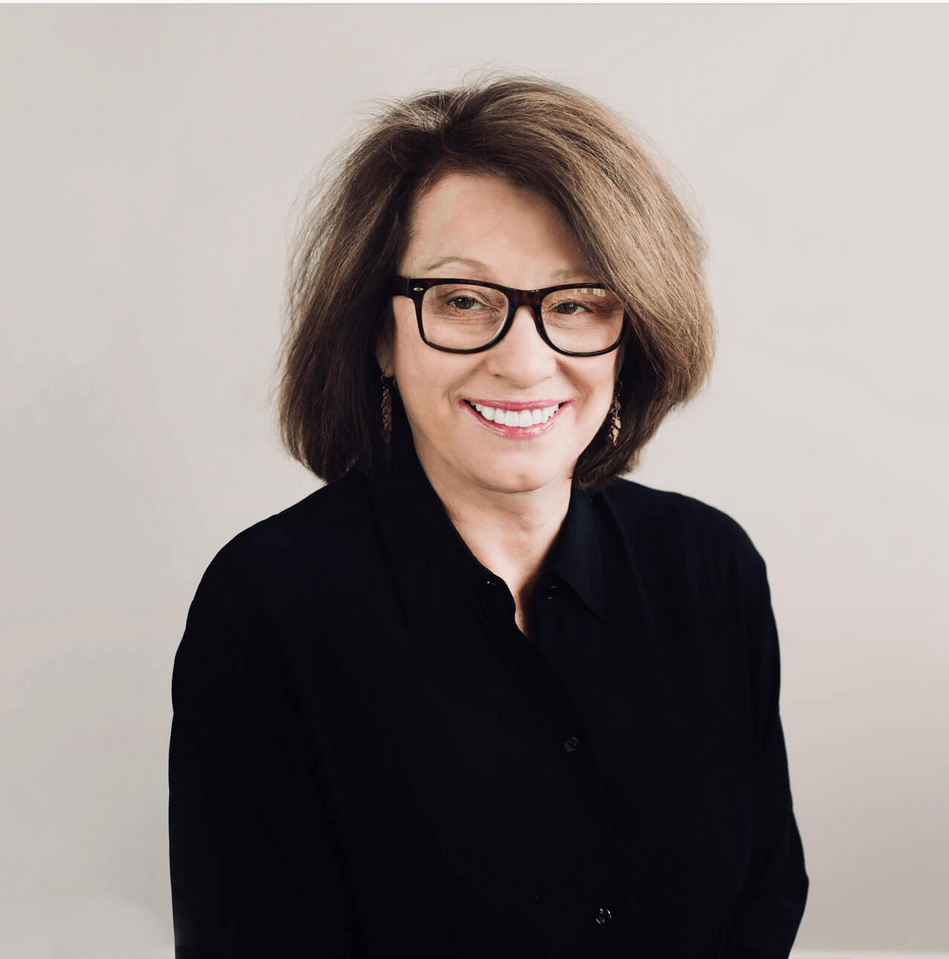 Professional headshot of a woman with glasses, smiling, wearing a black shirt.