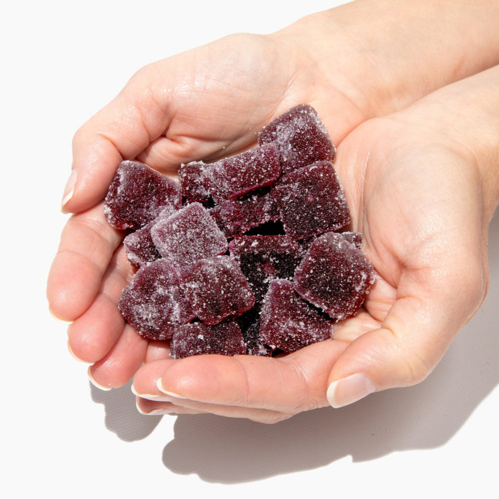 Hands holding purple gummy bears against a white background
