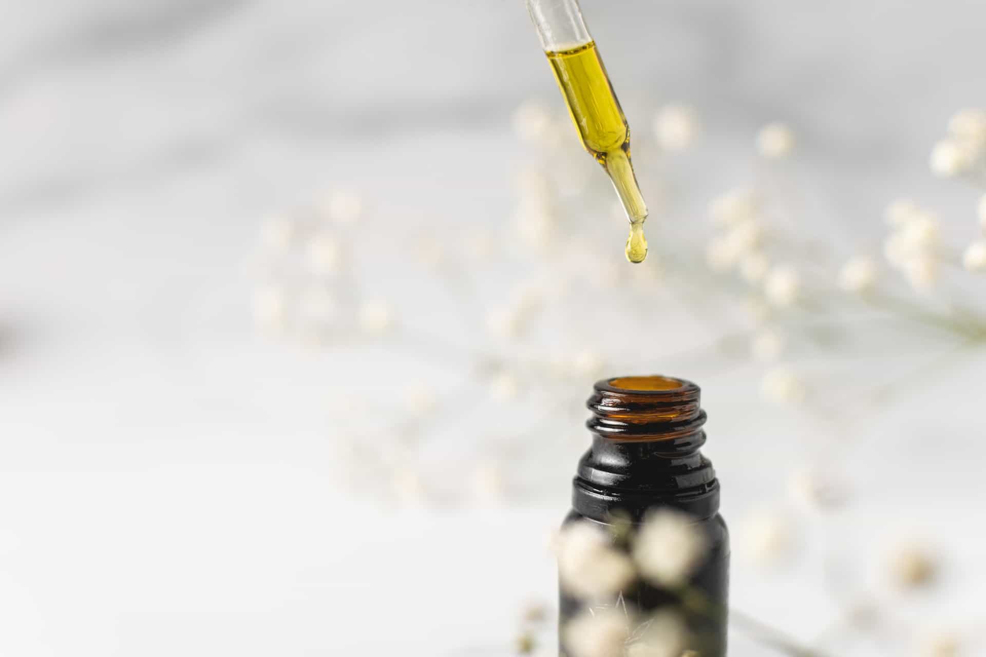 A dropper dispensing Delta-8 tincture from a dark glass bottle with white flowers in the background.
