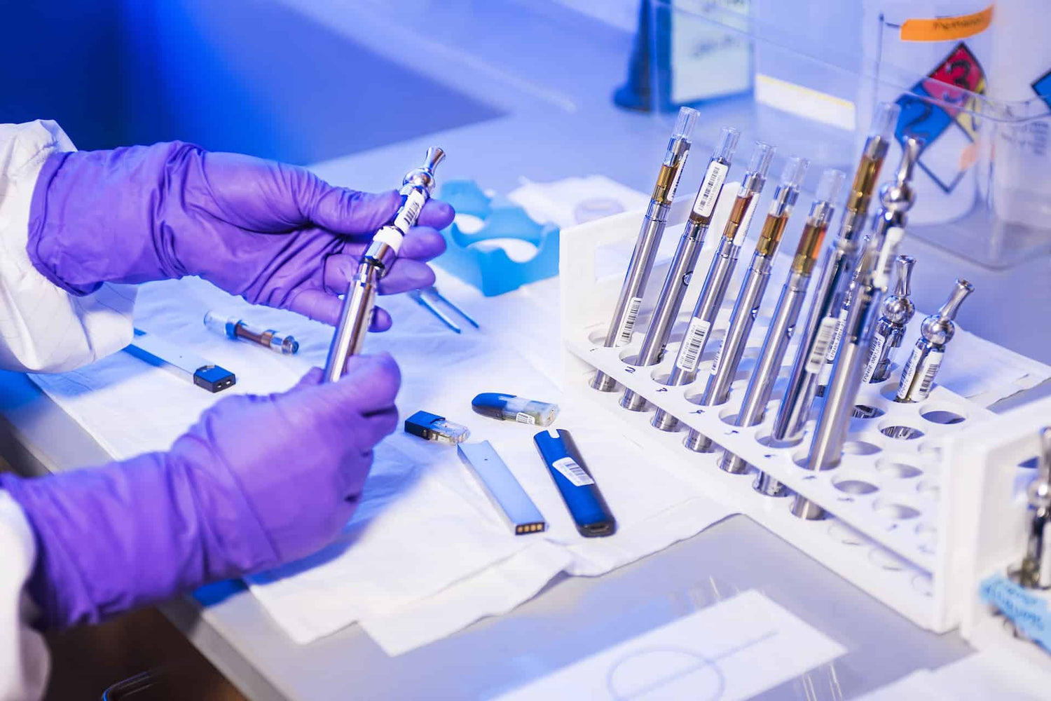 A person in gloves working on various vape cartridges on a table.