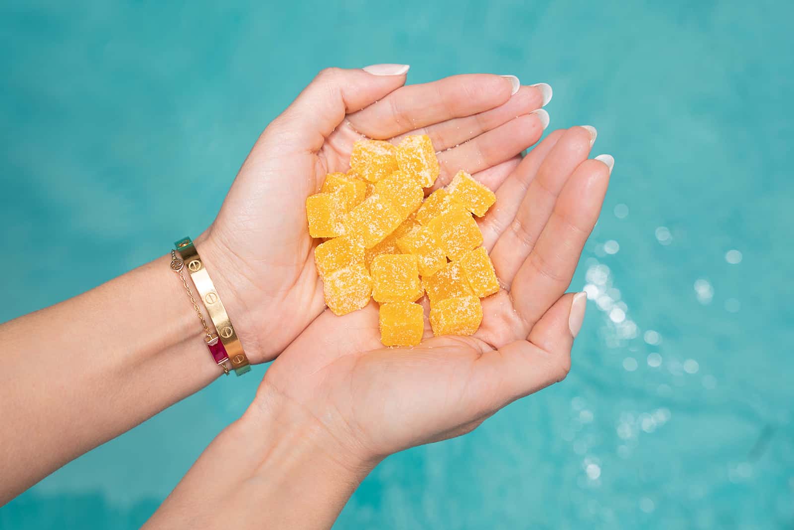 A person's hands holding a pile of yellow gummy candies against a blue background.