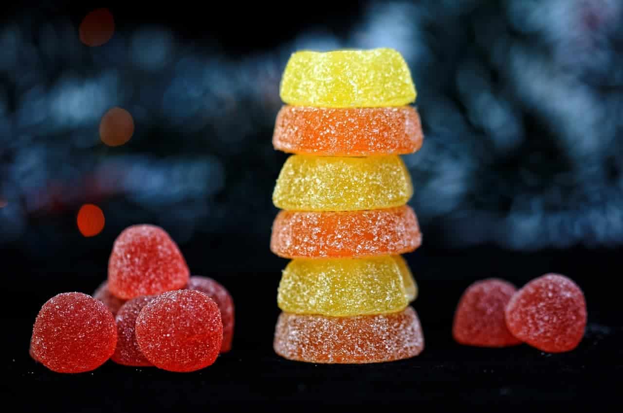 A stack of colorful gummy candies in various shapes and colors, including yellow and orange, with some scattered red gummies.