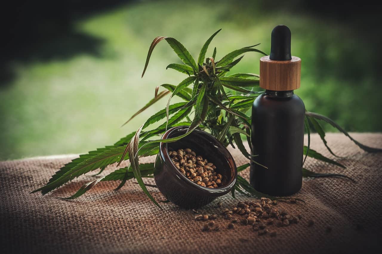 A dropper bottle next to hemp leaves and seeds on a table.