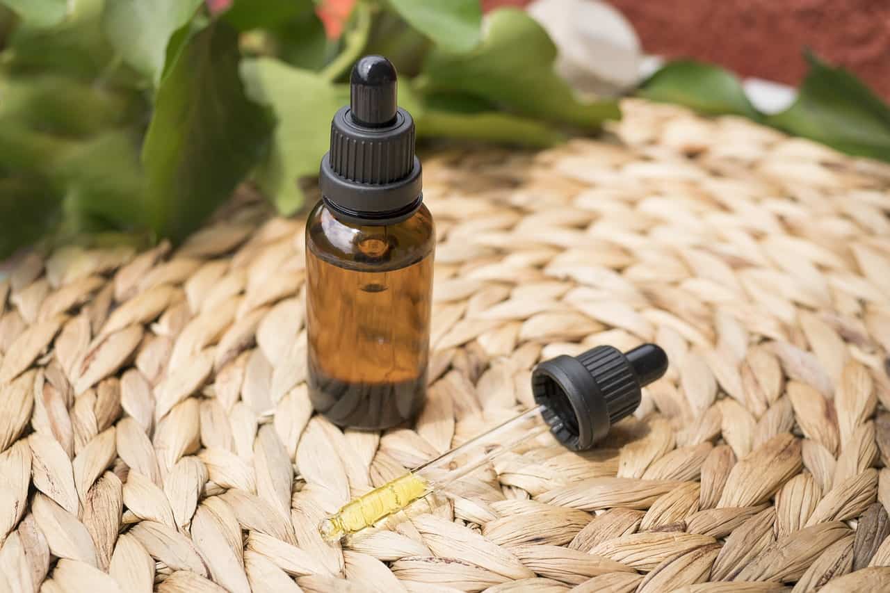 Amber dropper bottle with a dropper cap on a woven surface, surrounded by greenery