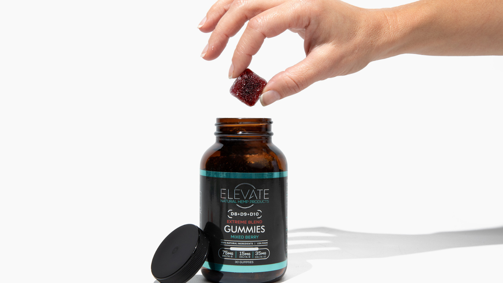 A hand reaching for a mixed berry gummy from an Elevate jar labeled 'Extreme Blend Gummies'.