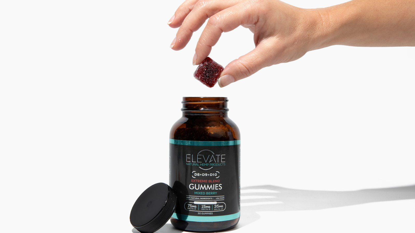 A hand holding a Delta 8 gummy from a jar labeled 'Elevate Delta 8 Gummies - Mixed Berry'