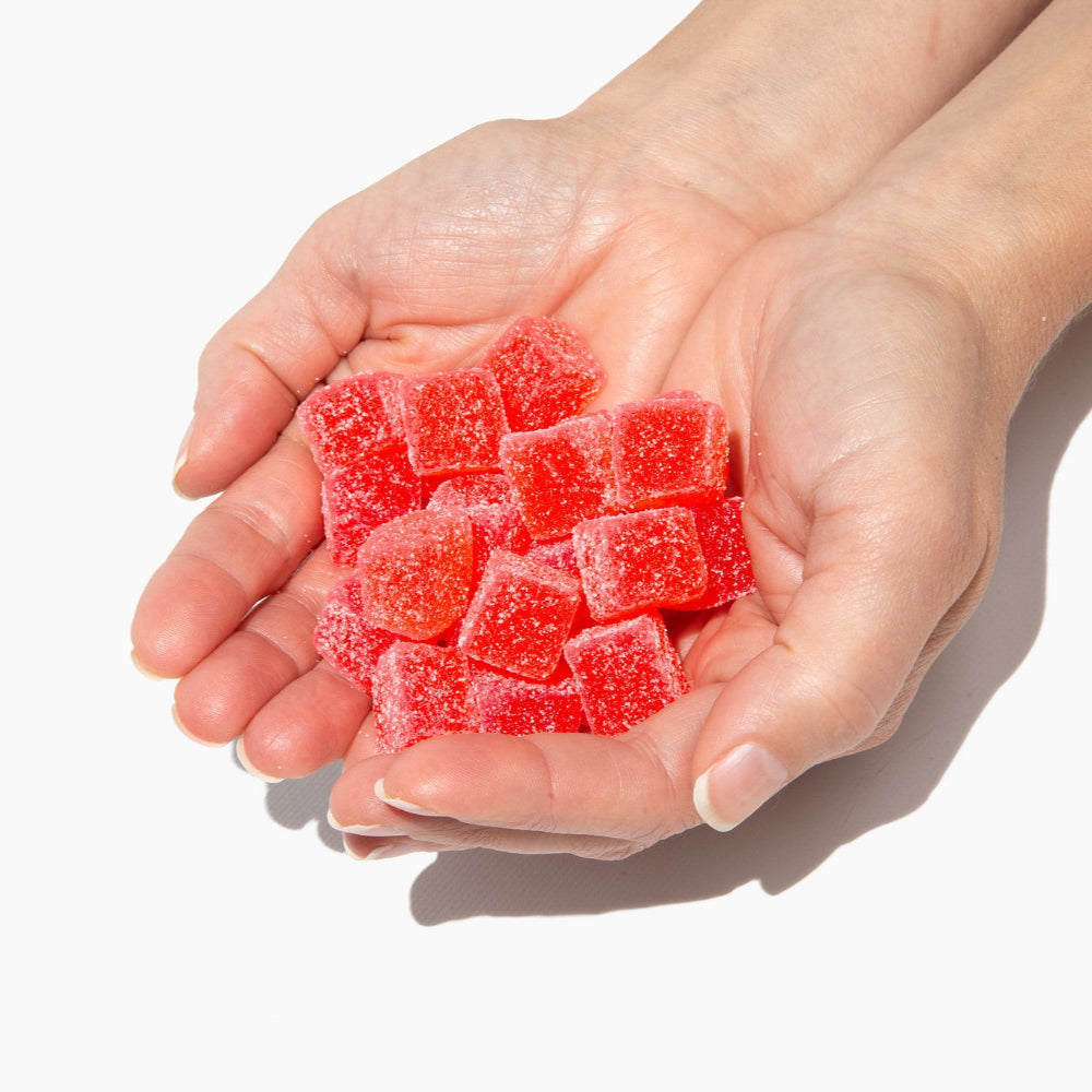Hand holding red gummy bears against a white background