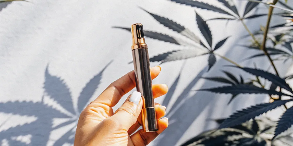 Hand holding a THCA pen in front of cannabis leaves, a top choice for buying pens online.